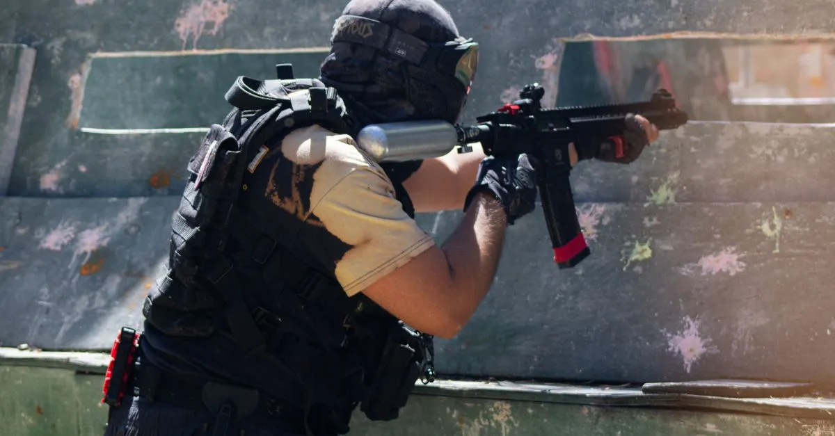 Woodsball player wearing a paintball vest and full gear while aiming outdoors