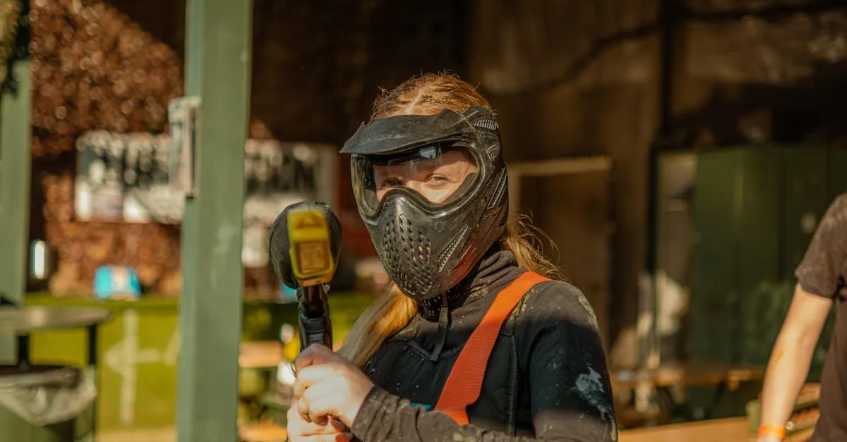 Young woman wearing protective paintball gear and mask posing with a paintball gun outdoors.